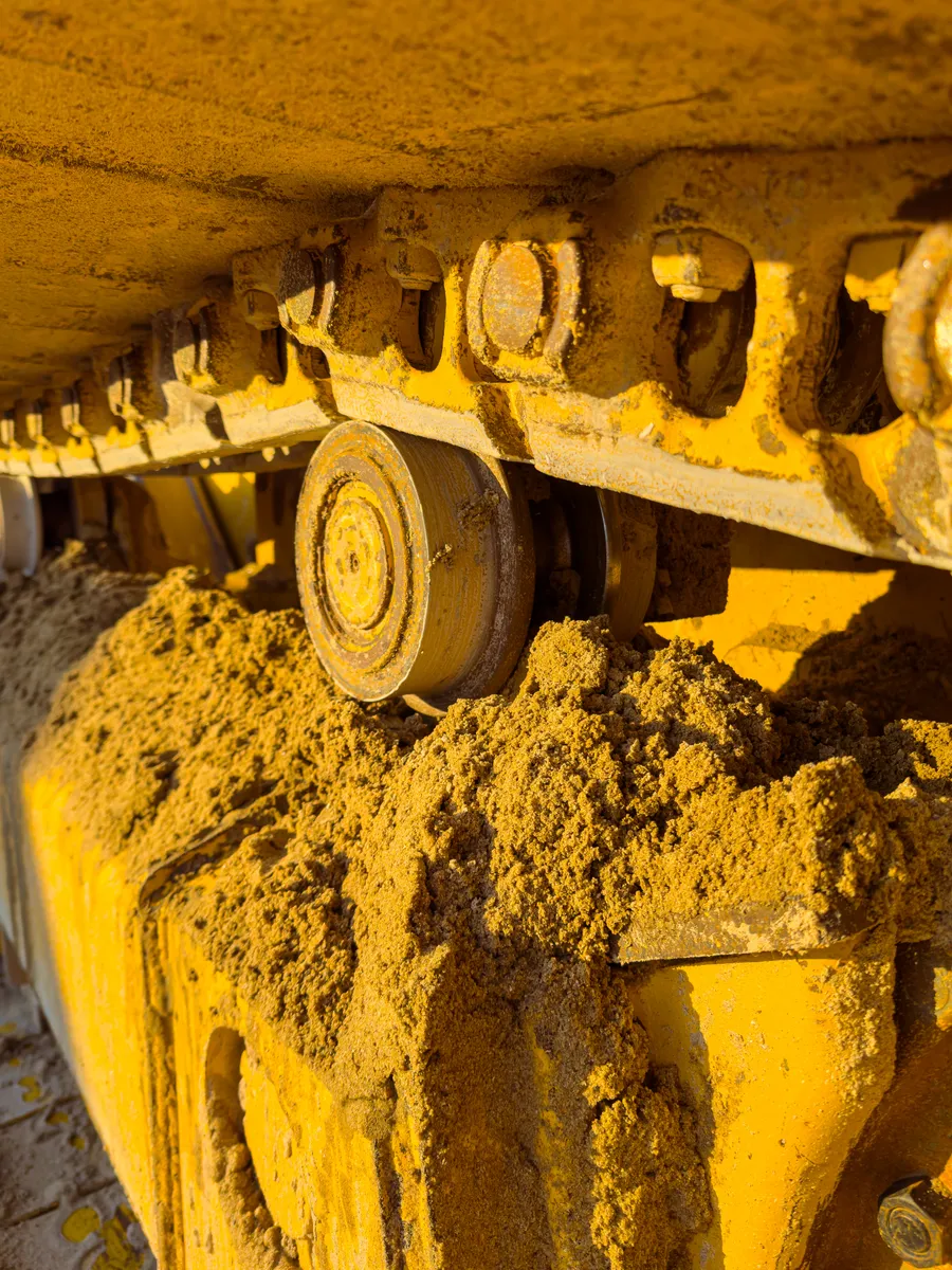 Close-up of a crawler machine's track rollers and links packed with mud